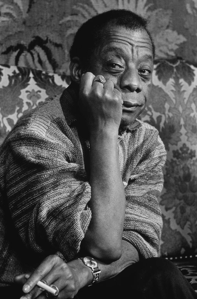 Black and white photograph of James Baldwin holding a cigarette. 