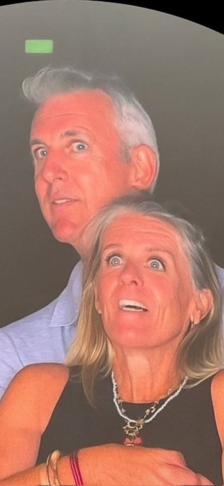 The CEO and CPO of Astronomer getting caught cheating on the Jumbotron at a Coldplay concert. The CEO is behind the CPO holding her. Both their faces have different expressions of surprise as they get caught having an affair in 4K. 