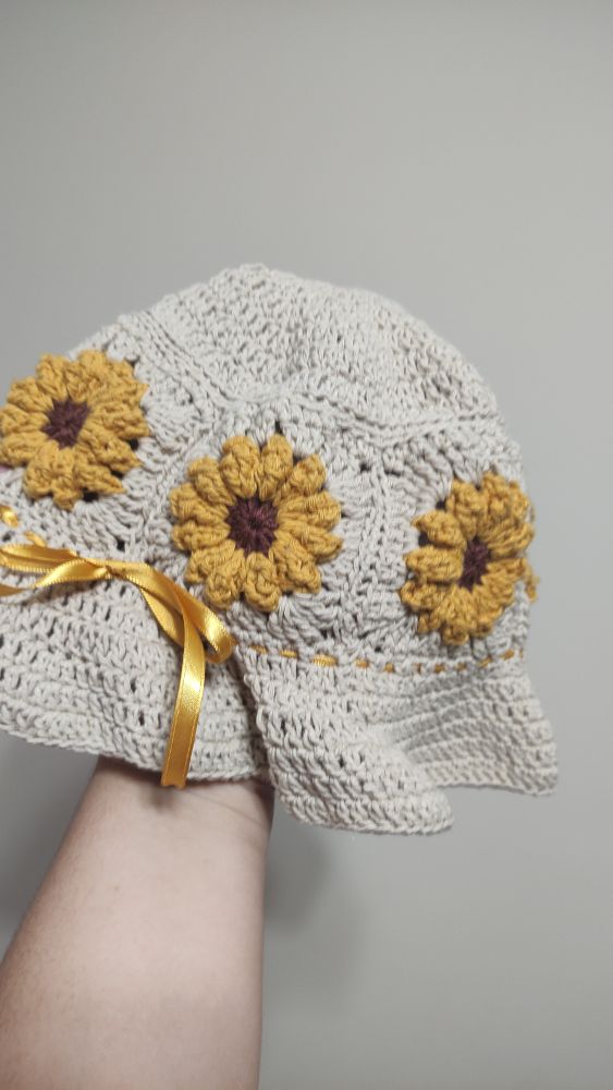 Chapéu com girassóis feito de crochê. Feito com linha crua, amarela e marrom. Tem um laço feito com fita de cetim na mesma cor das pétalas dos girassóis.
