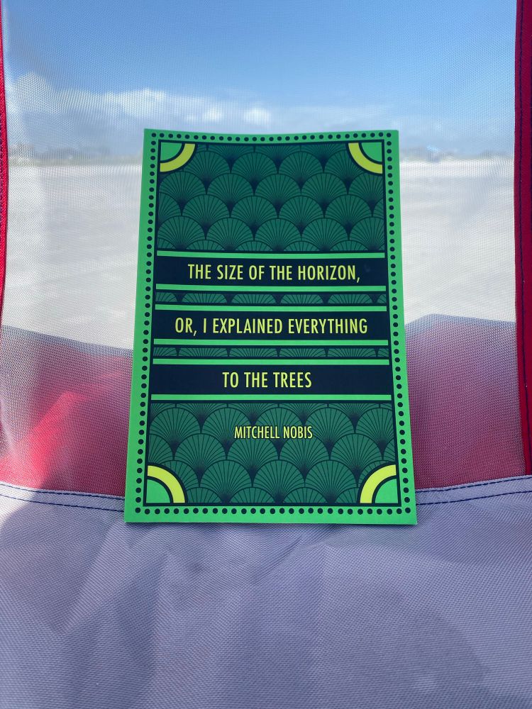 Mitch Nobis’ full length book (a gorgeous cover in green and yellow) resting on a beach lounger.