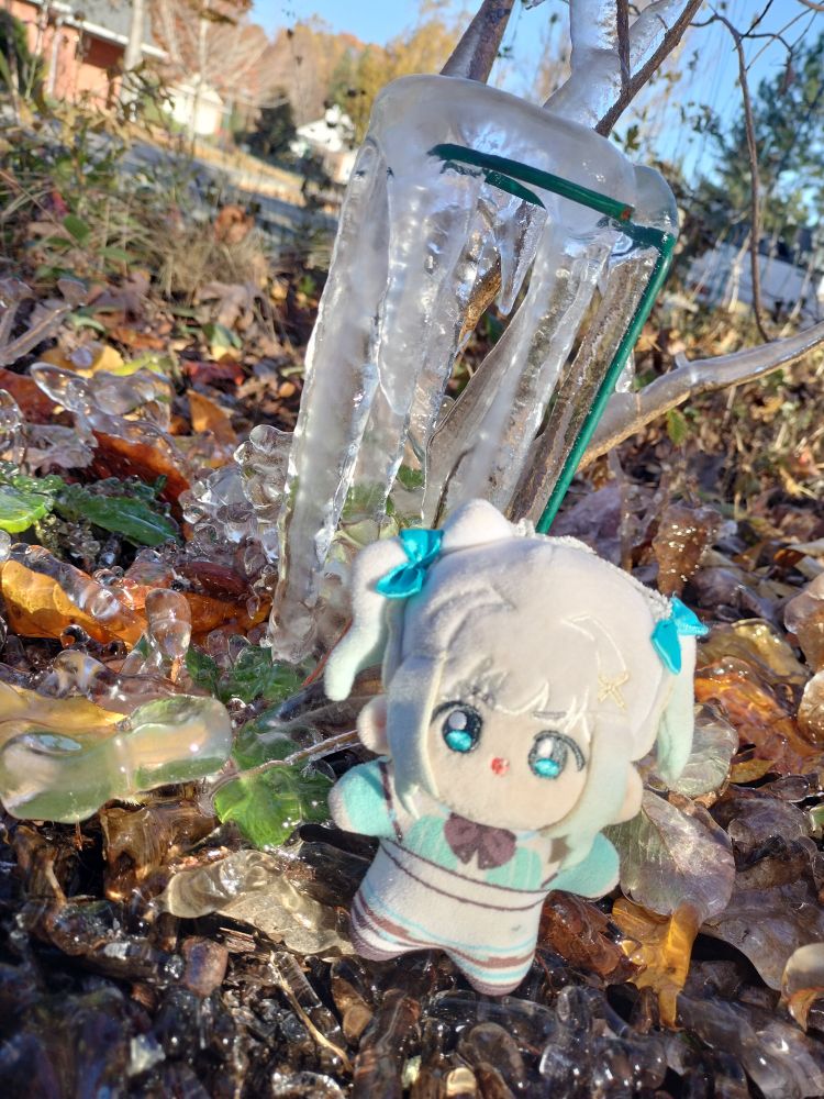 mint fantome plushie standing on the ground next to vegetation and a plant support covered in icicles and frost