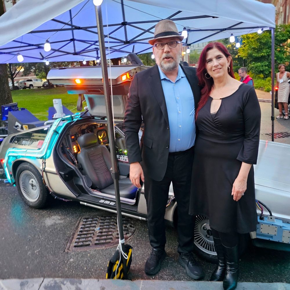Technodad and Demeter standing to the side of the BttF Delorean.