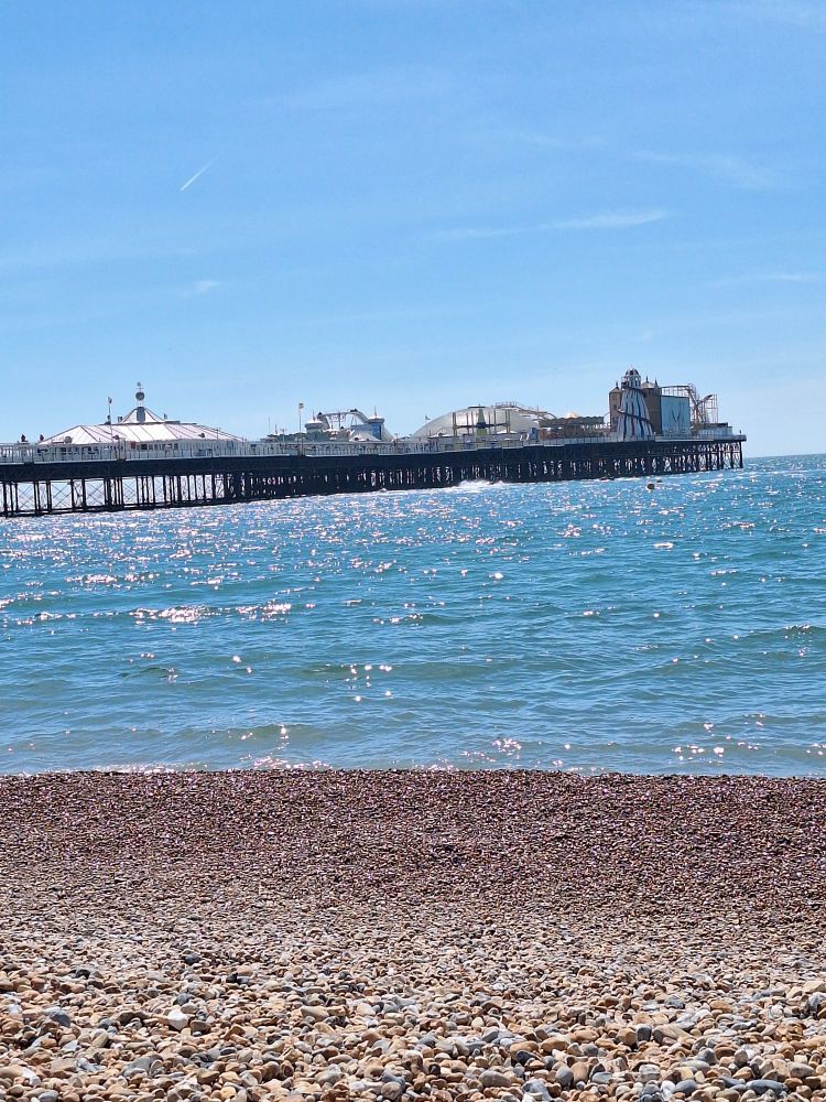 Brighton pier. Blue skies, sparkling blue sea and shingle beach.