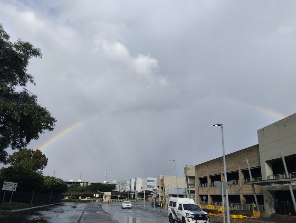 Rainbow showing arch with cloud covering top part of rainbow with rain in the distance 