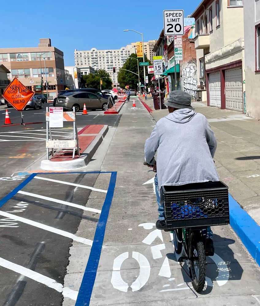 photo of a person wearing a hoodies and a cap, riding a bike with a large milk crate on the back along the 10th St protected bikeway in Oakland Chinatown