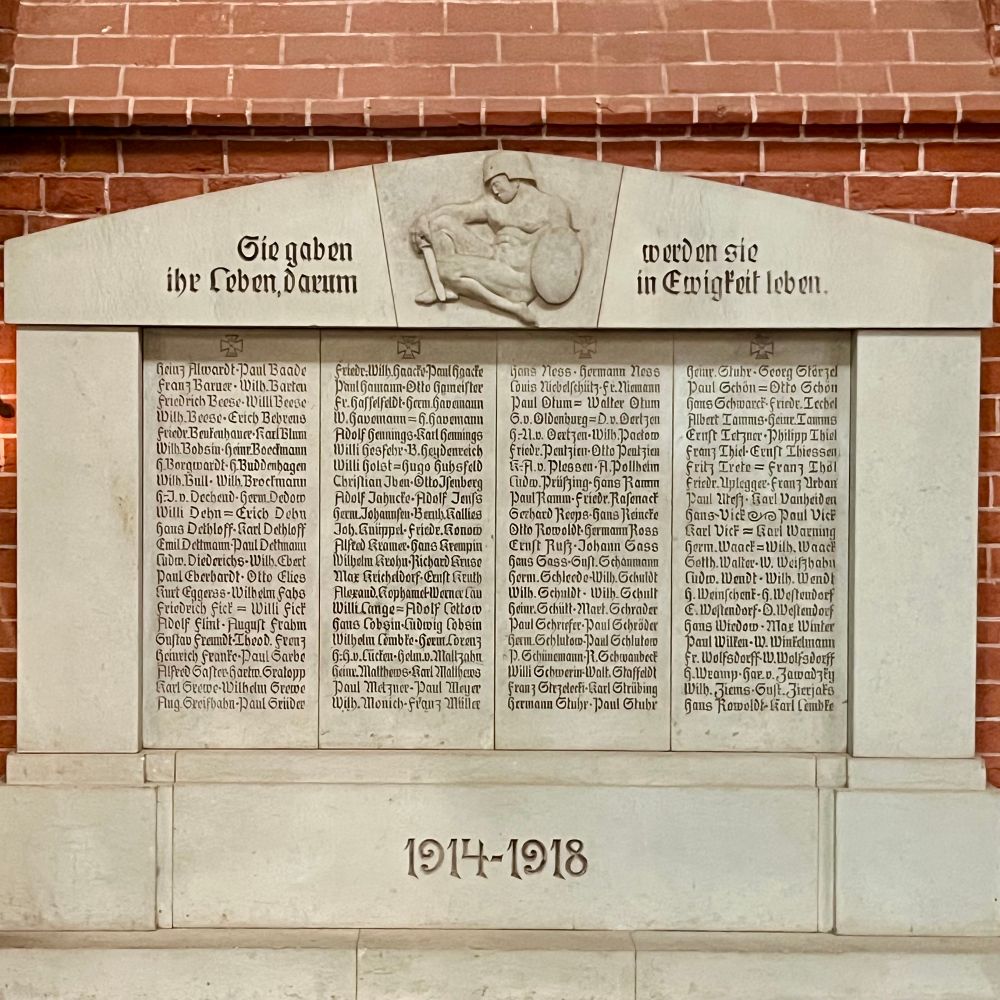 Weiße steinerne Gedenktafel mit eingravierten Namen. Darüber der Schriftzug „Sie gaben ihr Leben, darum werden sie in Ewigkeit leben“. Darunter der Schriftzug „1914-1918“.