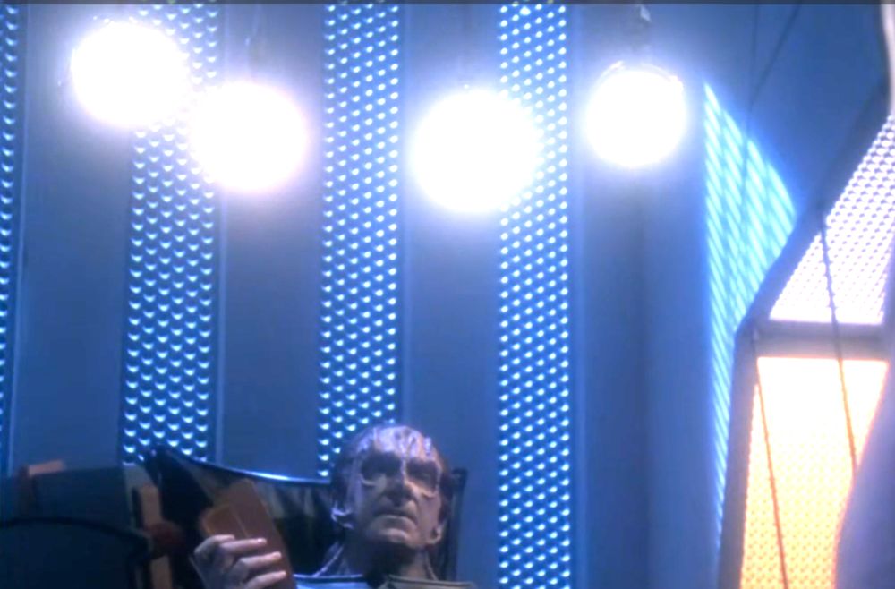 scene from star trek the next generation s06e11 "chain of command (part 2)" in which gul madred (pictured in the lower half), a cardassian interrogator, sits under four bright lights directed at his prisoner, captain jean-luc picard (not pictured)