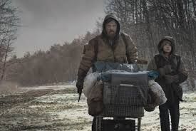 A still image from The Road where a haggard looking middle aged man and a young boy are walking through a desolate wasteland pushing a shopping cart