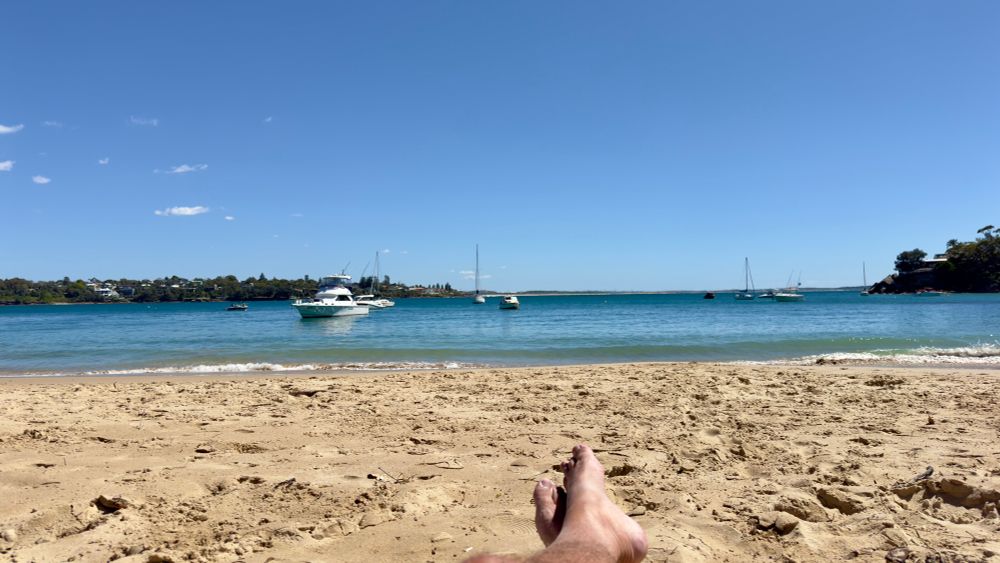 View from a pristine beach with blue sky and sea, looking onto a white boat floating nearby 
