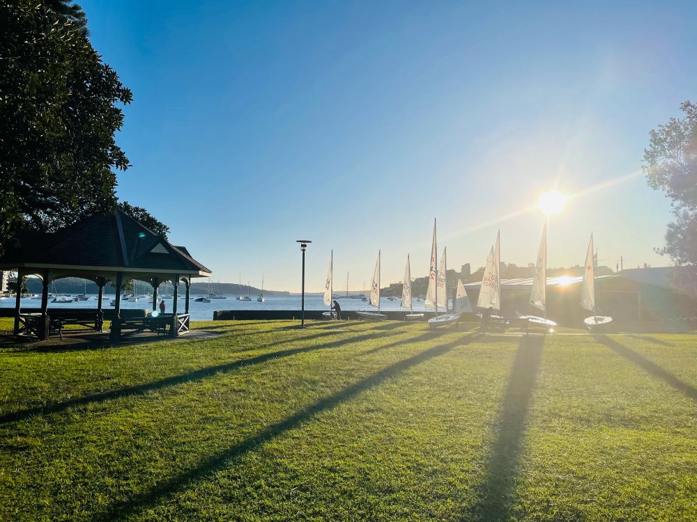 Small sailing boats lined up on the grass in front of double bay harbour in Sydney on a sunny morning 