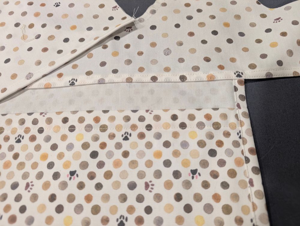 Inside fabric pieces for a tote bag, with the edges hemmed and a large pocket attached to one side. The fabric is decorated with cat-colored polkadots, interspersed with paw prints and mice