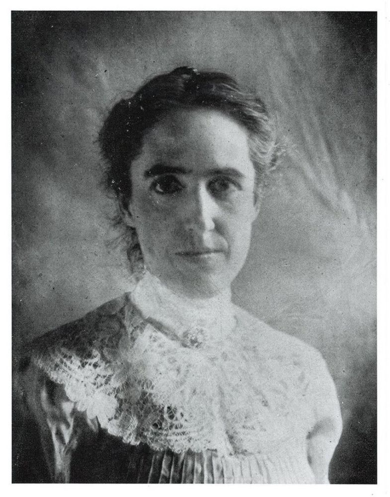 A black and white photograph of Henrietta Swan Leavitt. She is wearing a white blouse with a large lace collar that covers her shoulders, upper chest, and neck. Her hair is pulled up and she is looking directly at the camera. She has dark eyes in tis photo, strong eyebrows, and a long, thin nose. 