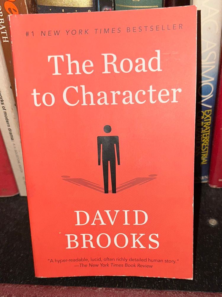 A red book with the words “The Road to Character” in white, and a black stick figure.