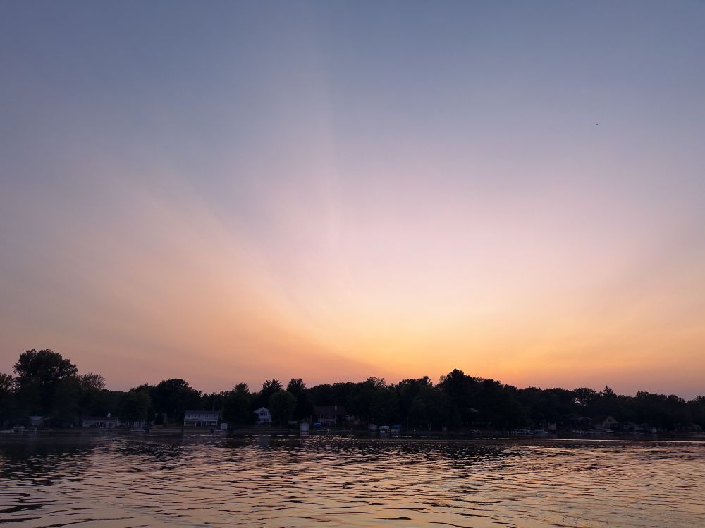 A rose and peach sunset through hazy skies, taken from out on a lake