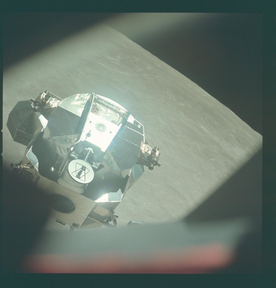 The lunar module detaching from the Command and Service Module, to begin its orbit around the moon. It is reflective and angular, with a small dish jutting prominently off one side and bright reflections on its surface.