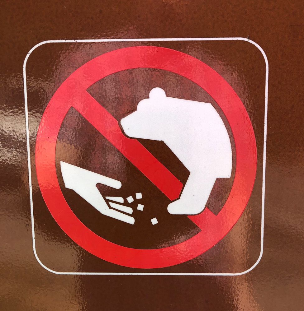 A sign that shows a bear and a human hand apparently dropping food in front of it. But it looks like the hand is rolling 4d6. There is a red circle with a slash around the whole thing, indicating that you should not do it.