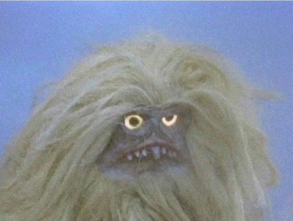 A weird snaggle toothed muppet with yellow eyes and a shock of white hair