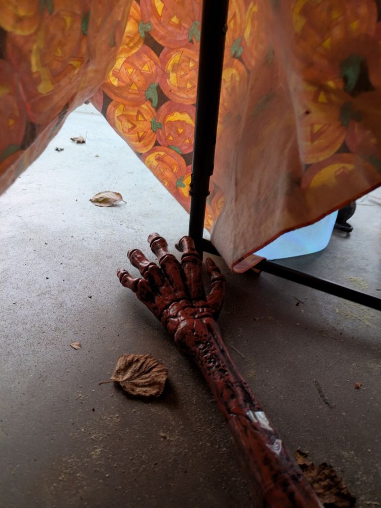 A skeleton hand taped to a yardstick
Picture is shot from beneath a table with pumpkin tablecloth