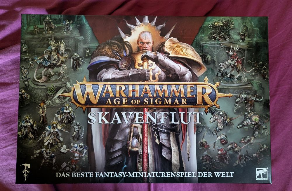 Foto der Verpackung des Tabletop-Spiels „Warhammer Age of Sigmar: Skavenflut“. Im Zentrum ist ein mächtiger Krieger der Stormcast Eternals mit goldenem Schulterpanzer und Schwert abgebildet. Um ihn herum sind zahlreiche Miniaturen zu sehen: links Armeen der Stormcast Eternals, rechts Skaven mit Rüstungen und Maschinen. Unten steht der Schriftzug „Das beste Fantasy-Miniaturenspiel der Welt“.

