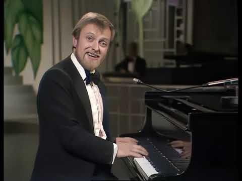 Ginger satirist Richard Stilgoe at the piano singing a whimsical song through his beard