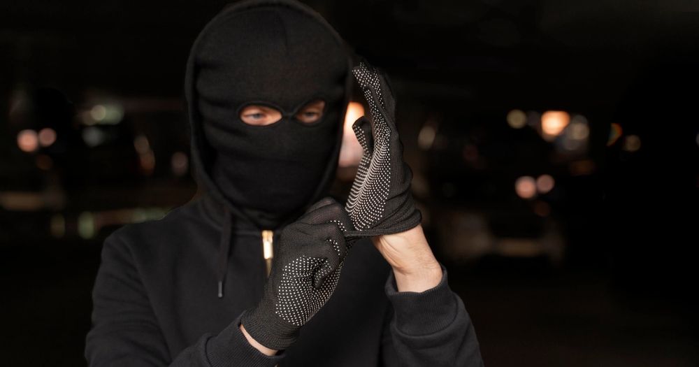 Burglar in ski mask and all black clothing putting on a pair of gloves at night.