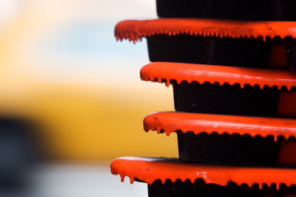 Das Bild zeigt einen oranger Stapel Verkehrsleitkegel. Die orange Farbe scheint an den Rändern der Kegel abzutropfen. Im Hintergrund ist ein sehr unscharfes gelbes Auto zu sehen.