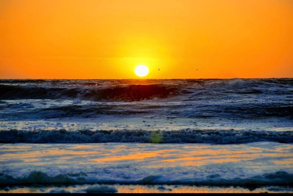 Sonnenuntergang an der Nordsee. der Himmel ist ein sattes orange gelb rot getaucht. Die Sonne ist kurz davor unterzugehen. Das Wasser brandet in einigen Wellen an den Strand.