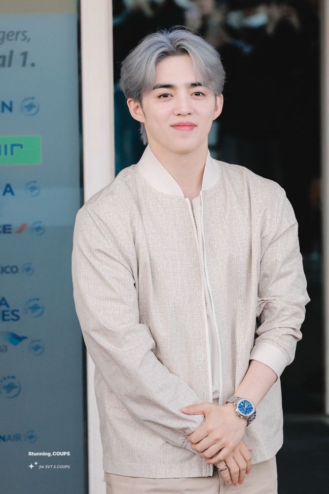 scoups wearing neutral on neutral. his hair is a blue grey. he is wearing a gold bracelet and silver watch. he is smiling.