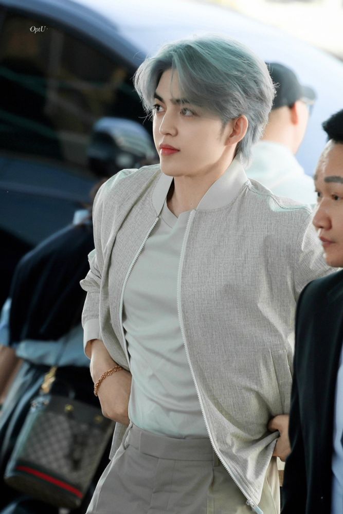 scoups wearing neutral on neutral. his hair is a blue grey. he is wearing a gold bracelet and silver watch. he is pulling up his pants.