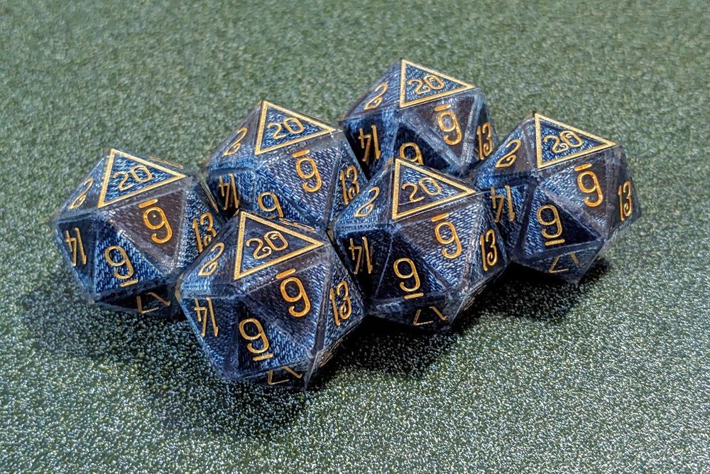 A set of 6j20 (six twenty-sided jeans dice). The denim texture is clearly visible (if wet in some spots) under the surface of the jice, and the numbers are painted gold.