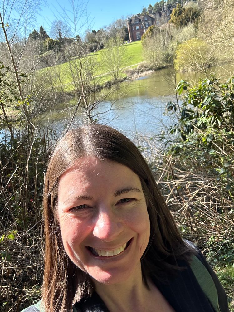 smiling brown haired woman standing in front of lake