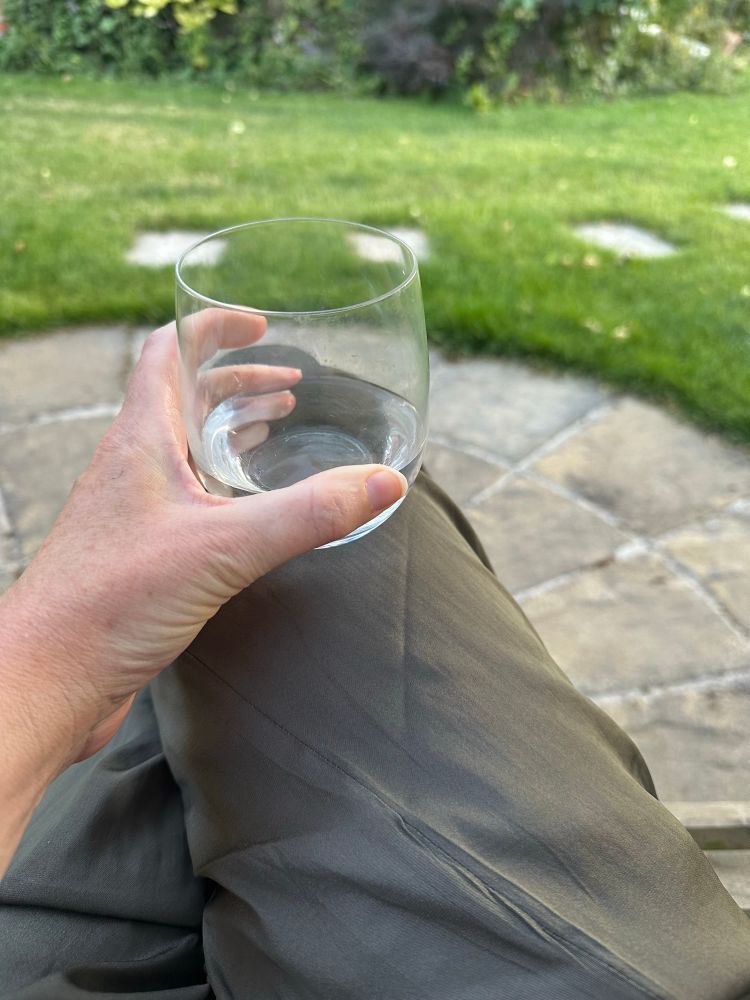 Glass of water balanced in a knee, in a garden 
