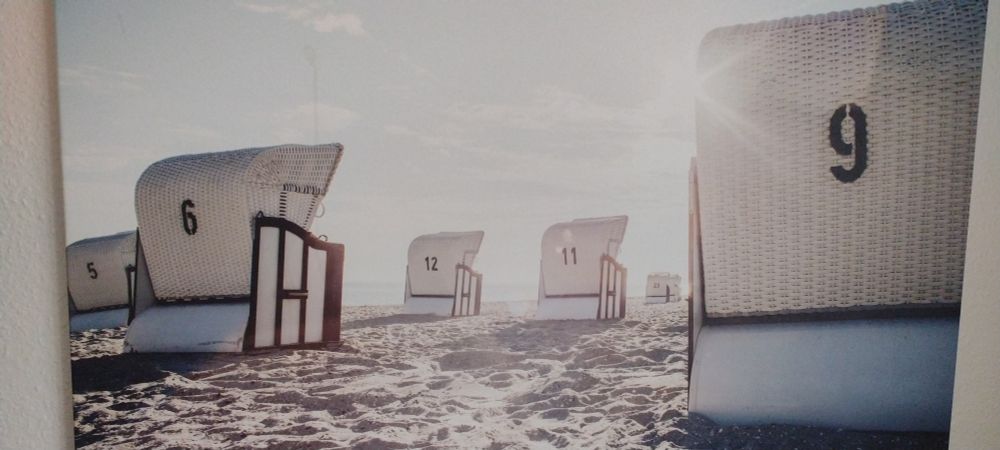 Ein an der Wand hängendes Bild vom Strand mit mehreren Strandkörben. Die Strandkörbe tragen Nummern: 5, 6, 12, 11, 23, 9.