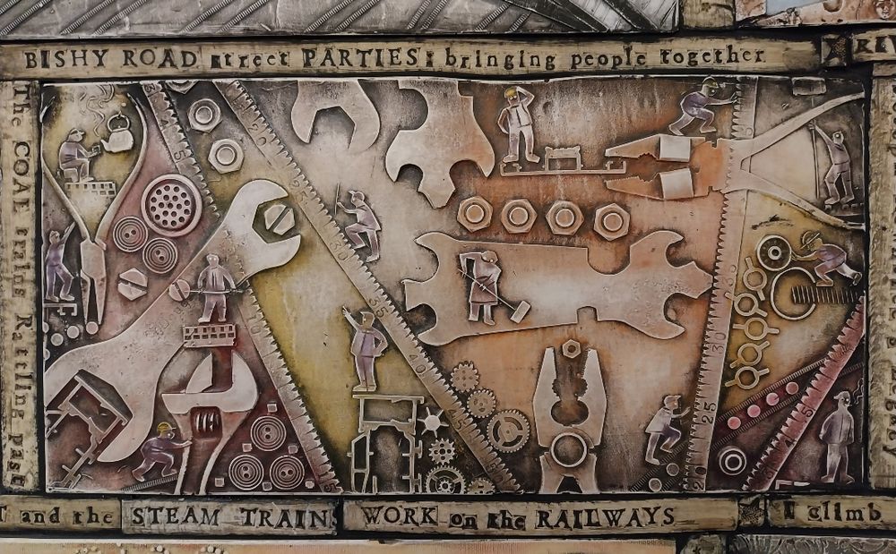 Mural with large gears, cogs, and tools, depicting construction workers building and operating machinery. Text references Bishy Road parties and railways.