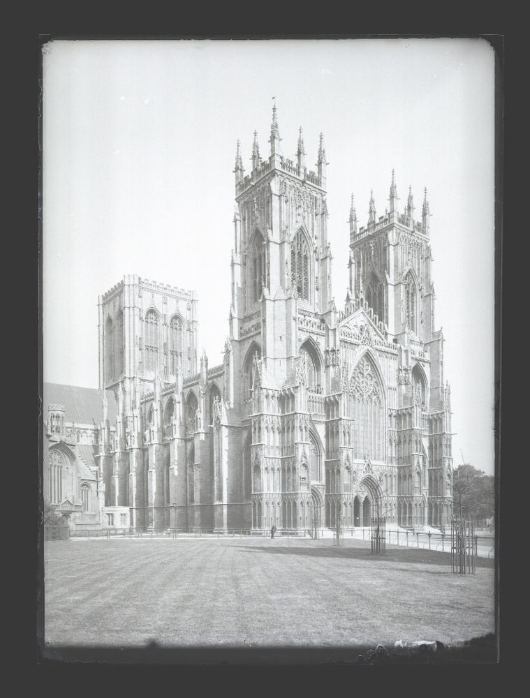 Exterior of York Minster and part of the Minster Gardens, c.1900

Gothic cathedral with two tall towers, intricate stone facade, and large arched windows, set against a clear sky and open lawn.
