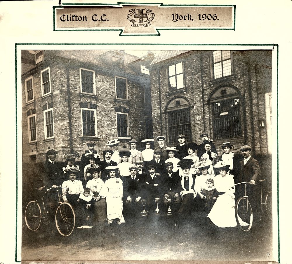 Clifton Cycling Club group photo from 1906, York. Men and women in formal attire with bicycles, trophies in front, posed outdoors.