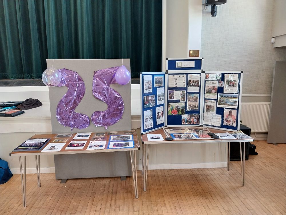 Display setup for a 25th anniversary event, featuring purple balloon numbers "25" and a board with photos and information about the history of York People First.