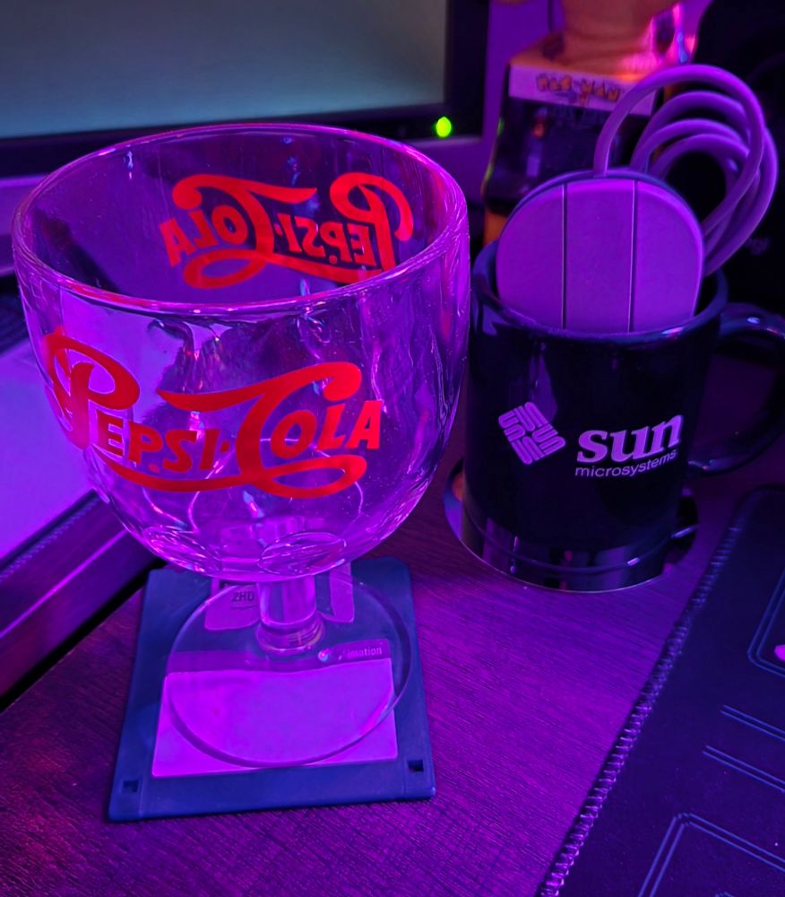 A Pepsi-Cola wide mouthed glass sitting atop a blue 2.5" floppy disk (left)
A dark blue Sun Microsystem mug with matching mouse sitting atop an HDD platter (right)