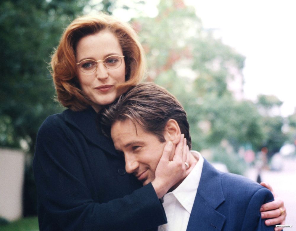 candid shot of Scully and Mulder, both smiling, his head tucked against her chest while she embraces him
