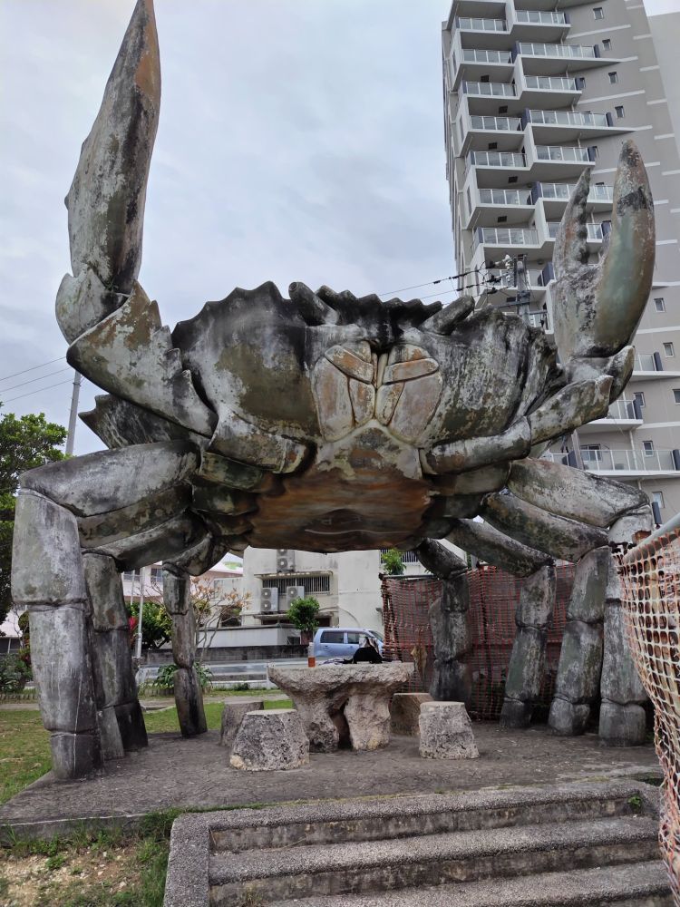 a stone table and chairs beneath a large crab statue, claws upraised in defiance of the gods 