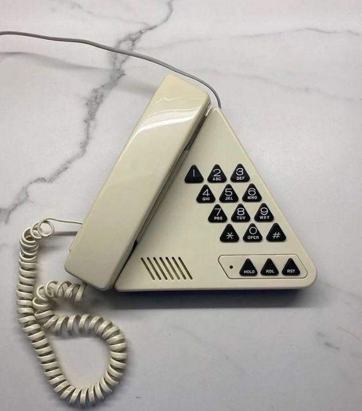 circa early 90's wired telephone, ivory colored in the shape of a triangle with triangular buttons sitting on a white marble surface 