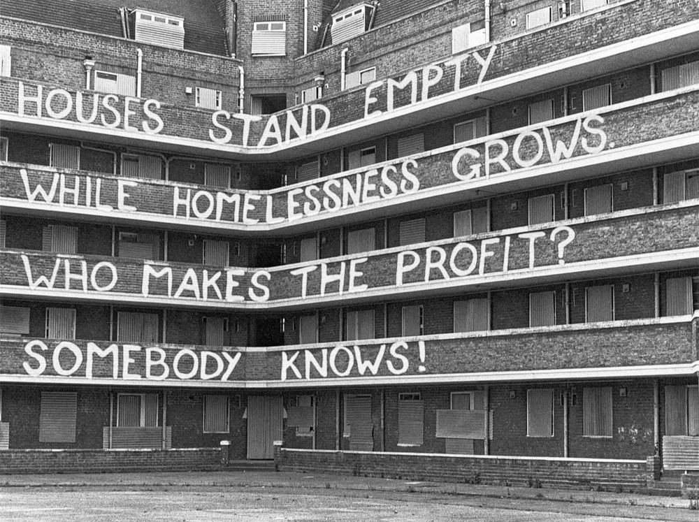 apartment block with graffiti on the walkway railings reading 

houses stand empty
while homelessness grows
who makes the profit?
somebody knows!