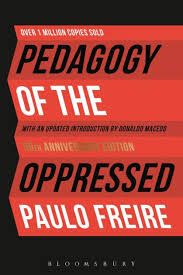 A cover of the Book Pedagogy of the Oppressed by Paulo Freire. Its a black background with a red paper that has accordion folds. The title and author's name are on the according folded paper