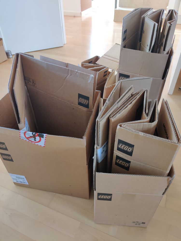 A pile of Lego cardboard boxes on the floor. 3 boxes of different sizes are open and contain other flattened Lego boxes inside them.