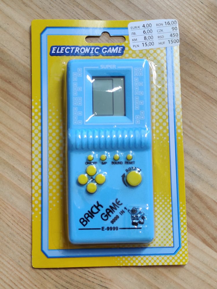 A light blue with yellow buttons "Brick Game" in packaging on a light wooden table. Price tag is €4.
Brick Game is a very popular Tetris knock-off from the 90s. This is the exact same build as then, labels/branding in all.