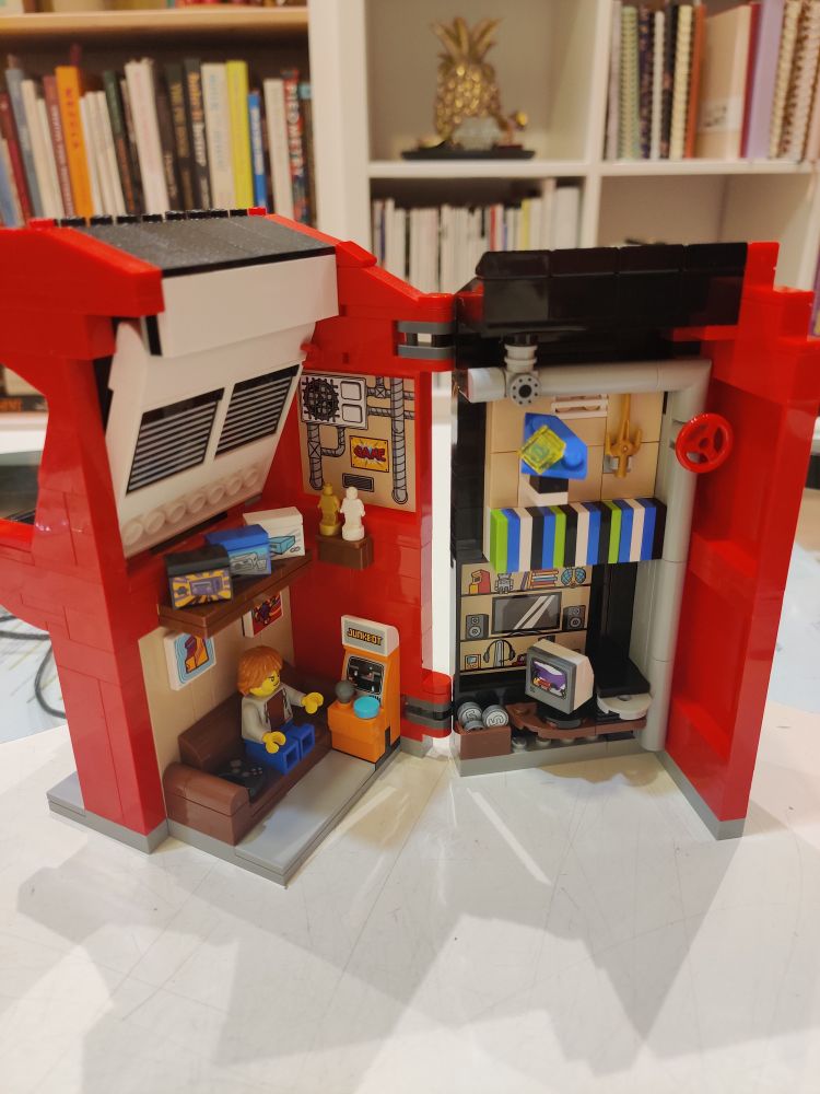 Lego arcade machine set on a table opened up showing the inside with a bookshelf in the background