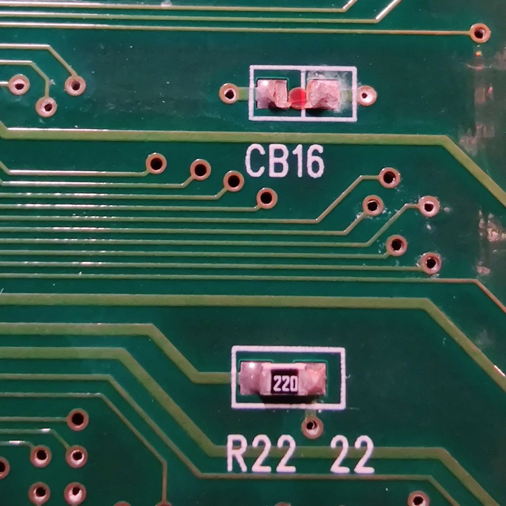 Close up of a IGS PGM rev5 PCB (bottom side) showing a missing CB16 component. It seems to have been ripped off judging by the shape of the leftover solder.