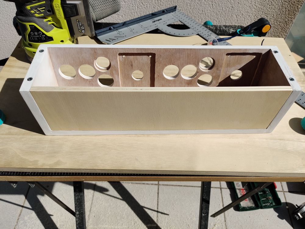Arcade control panel laying on its front side on a foldable worktable. The control panel is mostly white with a new unpainted bottom panel placed for sizing.