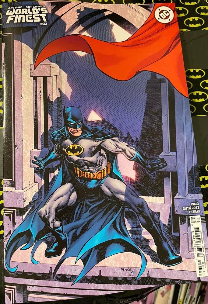 Batman stands on a ledge a shadow made by Superman falls across him.
