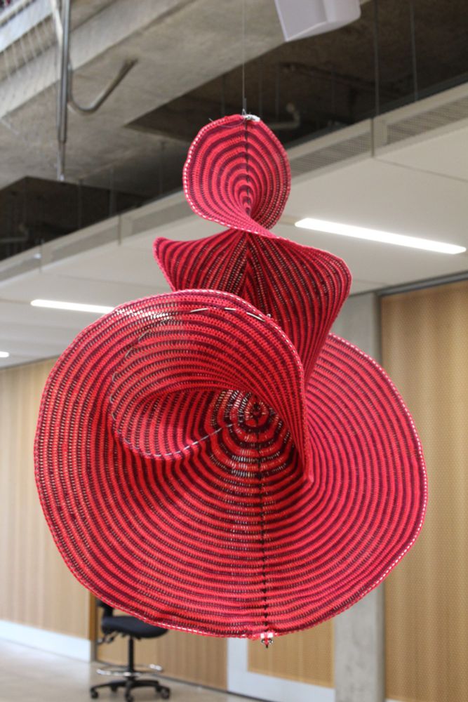 A red curved surface made from crochet with wire to give the edges definition, suspended from the top.